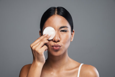 Shot of beautiful woman removing makeup while taking care of her skin while looking at camera on isolated backgroundの写真素材