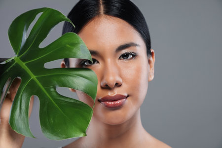 Shot of beautiful young woman posing to camera with a plain leaf on isolated gray backgroundの写真素材