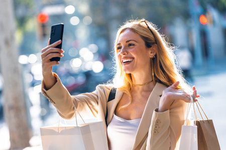 Shot of happy woman doing a video call with smartphone while carrying shopping bags walking through the cityの写真素材