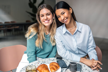 Shot of two beautiful women friends looking at camera while having breakfast in a coffee shopの写真素材