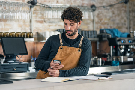 Shot of handsome waiter taking inventory of everything missing while making a checklist on his phone...