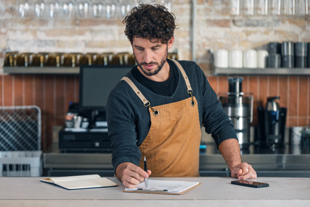 Shot of handsome waiter taking inventory of everything missing while doing a checklist at the coffee...
