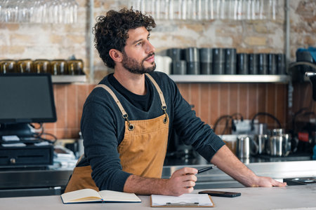 Shot of handsome waiter taking inventory of everything missing while doing a checklist at the coffee shopの写真素材