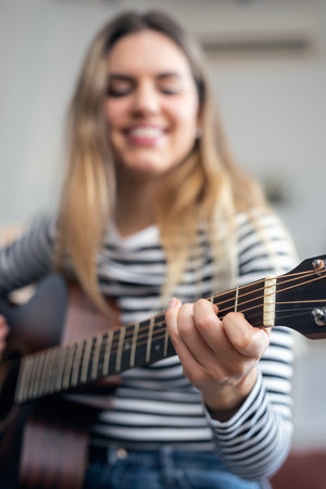 Shot of pretty influencer woman playing guitar and strumming in the living room at home