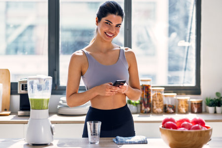 Shot of sporty young woman making a vegetable green smoothie while using smartphone in the kitchen at home.の写真素材