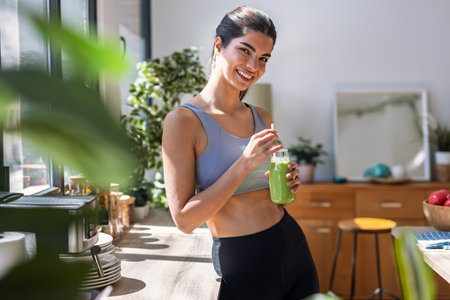 Shot of sporty young woman drinking a vegetable green handmade smoothie in the kitchen at home.の写真素材