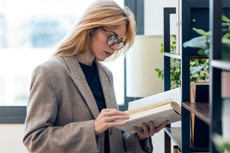 Shot of beautiful lawyer woman reading a book while standing in her modern office