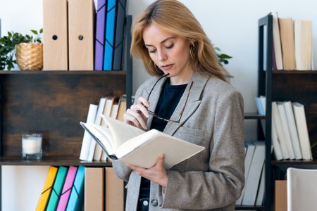 Shot of beautiful lawyer woman reading a book while standing in her modern office