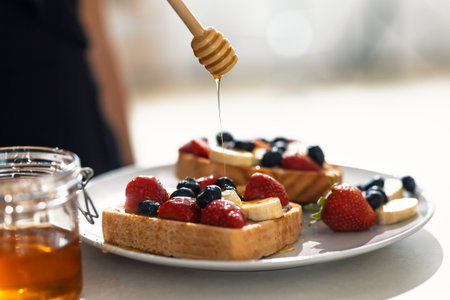 Close up of healthy delicious toasts with fruit served on a plate while honey is being drizzled over...