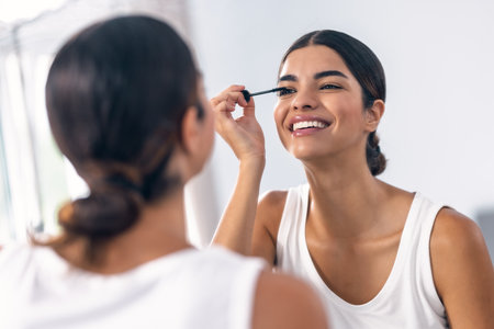 Shot of beautiful and smiling woman applying eyelash mascara in front of the mirror in the bathroomの写真素材