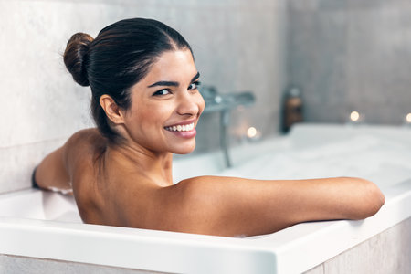 Shot of beautiful woman relaxing in the bathtub while looking at camera in the bathroom at home