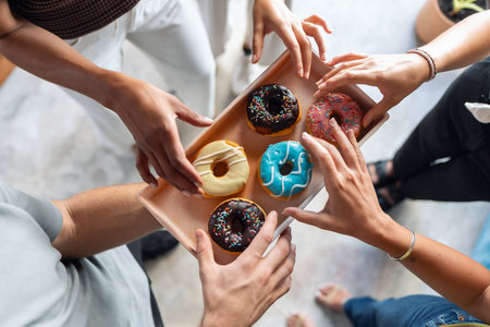 Shot of business people eating colorful donuts while taking a break from work in a coworking placeの写真素材