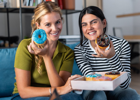 Shot of business people eating colorful donuts while taking a break from work in a coworking placeの写真素材