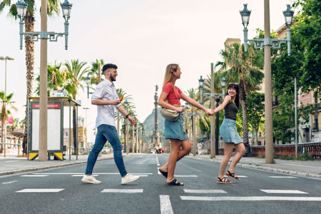 Shot of three happy friends walking across the crosswalk while sightseeing around the city in the summerの写真素材