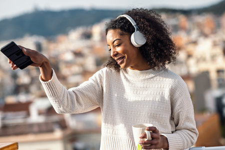 Shot of stylish woman drinking a cup of tea while dancing and listening to music with headphones on...