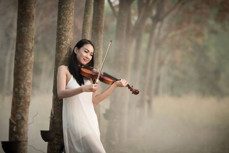Young beautiful woman playing violin in the forest.の写真素材
