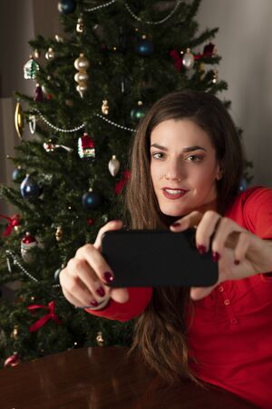 Pretty girl in red blouse looking at smartphone camera while making selfieの写真素材