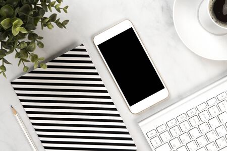 Close up on a white marble office desk with notebook, mobile, keyboard, mouse and a green plantの写真素材