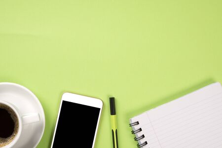 Top view from a light green color desk with stationery supplies, mobile and a coffeeの写真素材