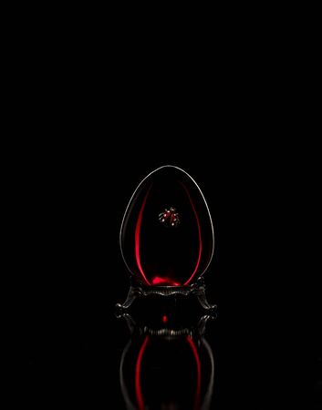 Red glass easter egg on a silver base on a black backgroundの写真素材