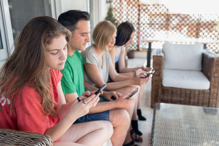 Family Sitting on a Sofa at the Balcony on addicted moment using mobile smart phonesの写真素材
