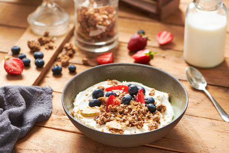 Healthy Breakfast with Glass of Milk and a Bowl with Fresh Granola, Muesli with Yogurt, Berries, Strawberries on a Wooden Table on Wooden background with Berries, Granola on it. Side Viewの写真素材