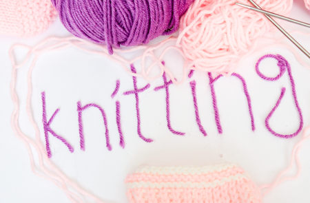 Written knitting with violet yarn, pink white and violet woolen skeins and knitted pieces の写真素材