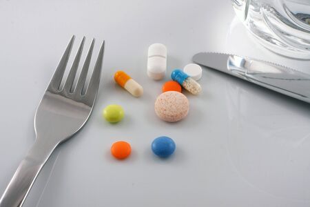 Medicine capsules and pills on dining plate with fork and knife. Signifying drug addiction, healthy eating and lifestyle, dieting and slimming, and healthcare concepts.の写真素材