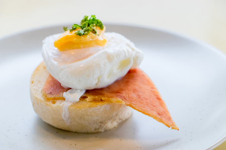 The Close up Breakfast is Egg Benedict on white plate. Eggs Benedict- toasted Thai muffins, ham, poached eggs, Spinach style.の写真素材