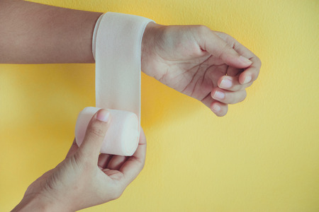 Medicine bandage on injury female wrist on yellow backgroundの写真素材