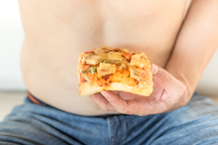 Unhealthy fat young man holding pizza fast food.の写真素材