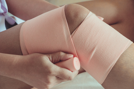 Medicine bandage on injury female knee on yellow background.の写真素材