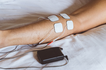 Patient applying electrical stimulation therapy on leg. Electrical tens.の写真素材