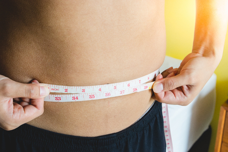Young man measuring waist line with measuring tape. dieting concept.の写真素材