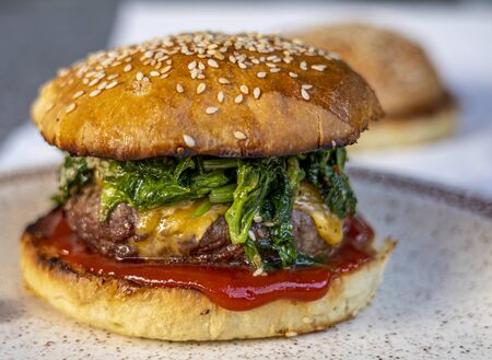 cheeseburger with beef patty, spinach, red sauce, cheddar cheese piled up in a self-made bun with sesameの写真素材