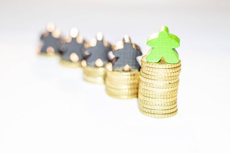Meeple on pile of coins with other meeples in the backgroundの写真素材