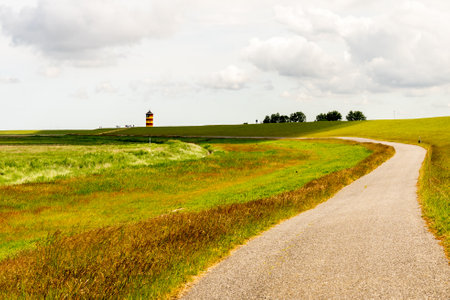 View on Pilsum lighthouse in East Frisia with tourists walking around the dike and taking photographsの写真素材