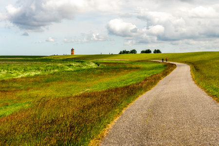 View on Pilsum lighthouse in East Frisia with tourists walking around the dike and taking photographsの写真素材