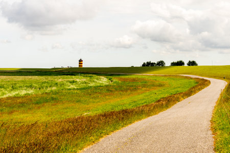View on Pilsum lighthouse in East Frisia with tourists walking around the dike and taking photographsの写真素材