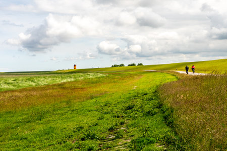 View on Pilsum lighthouse in East Frisia with tourists walking around the dike and taking photographsの写真素材