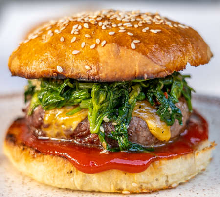 cheeseburger with beef patty, spinach, red sauce, cheddar cheese piled up in a self-made bun with sesameの写真素材