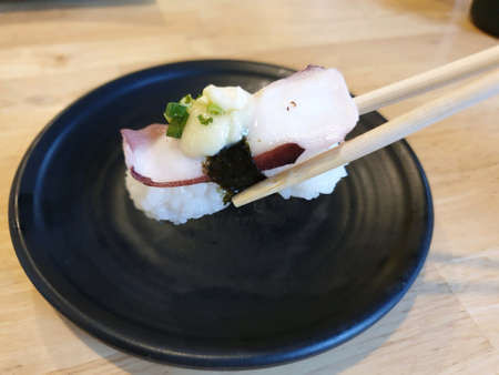 Chopstick holding fresh octopus sushi on black plateの素材