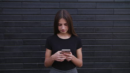 An attractive young lady wearing glasses using a phone against a brick wall background. Close-up...