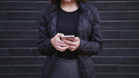 An attractive young lady wearing glasses using a phone against a brick wall background. Close-up shot 4kの写真素材