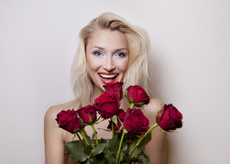 Smiling beautiful blonde woman posing with red roses. Girl with toothy smile.の写真素材