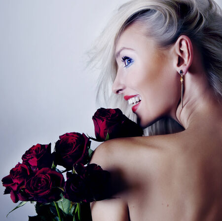 Smiling sensual blonde woman posing with red roses. Girl with toothy smile.の写真素材