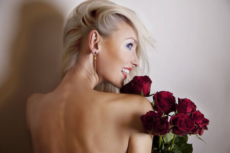 Smiling sensual blonde woman posing with red roses. Girl with toothy smile.の写真素材