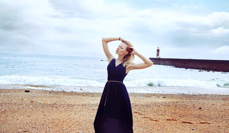 Portrait of beautiful blonde woman posing on beach in fashionable blue dress の写真素材