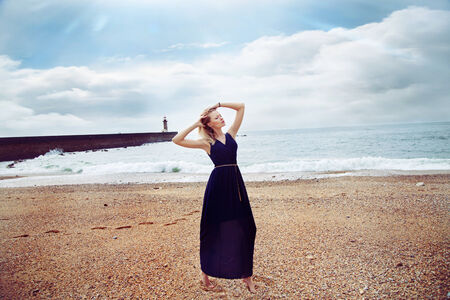 Fashionable young beautiful blonde woman posing on beach, wearing long dress の写真素材