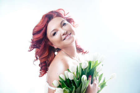 Beautiful redhead woman smiling, looking at camera. Attractive lady posing with white flowers.の写真素材